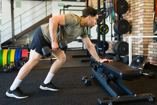 Person performing a dumbbell row with correct form in a gym setting, demonstrating proper strength training technique.